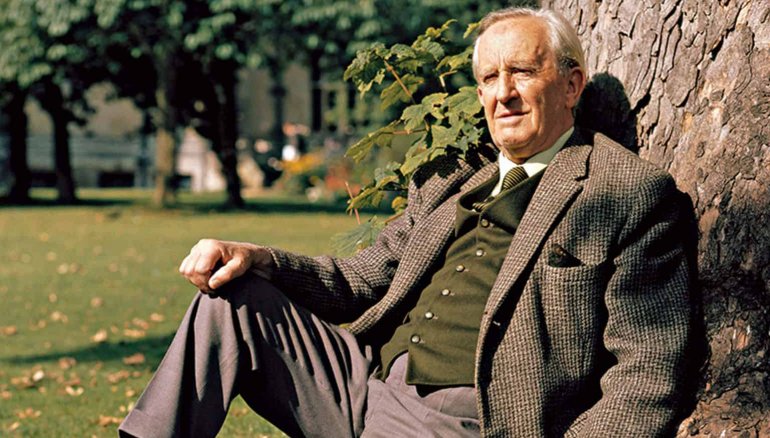 Foto de JRR Tolkien, ya de edad avanzada, sentado en la hierba junto a un árbol
