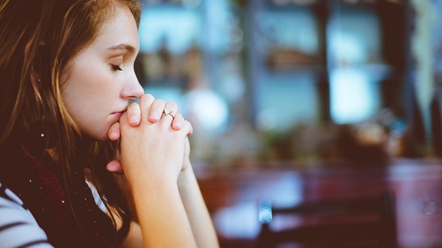 Una mujer en oración, con las manos unidas, en la iglesia