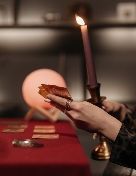 Una mujer sostiene cartas de adivinación en una mano y una vela encendida en la otra.