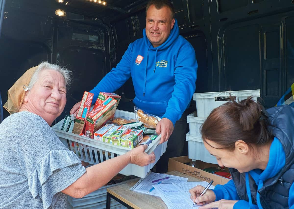Un voluntario de Cáritas Ucrania reparte paquetes de ayuda a una señora de edad avanzada