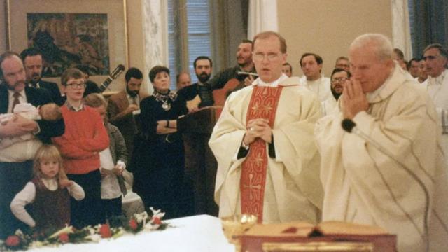 El cardenal Cordes, junto a Juan Pablo II en una celebración eucarística en Castelgandolfo, el 28 de diciembre de 1986. Detrás de Cordes, con una guitarra, canta Kiko Argüello. Cercana a él, Carmen Hernández.