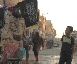Foto de agencia de un niño en Raqqa en octubre de 2013, ante un tenderete de uniformes y banderas yihadistas