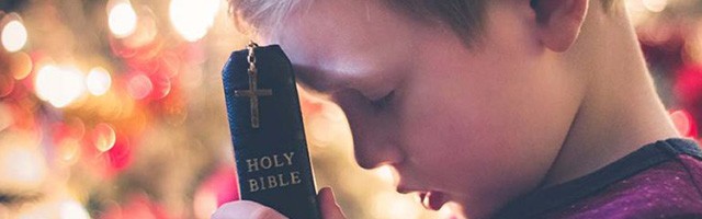 Un niño pequeño reza con la Biblia en las manos.