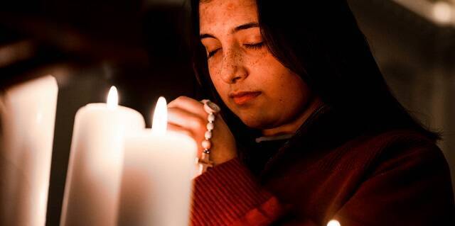 Una joven reza el rosario entre velas