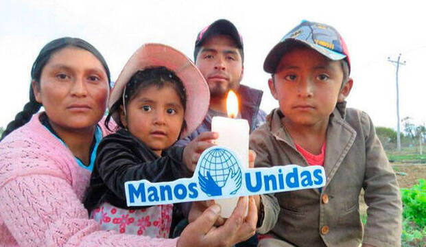 Niños sudamericanos con una vela y el cartel de manos Unidas