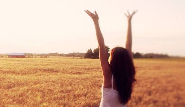 Una joven alza los brazos en actitud de alabanza en un campo soleado