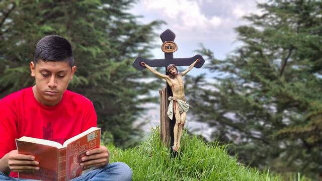 Un joven lee la Biblia junto a un crucifijo.