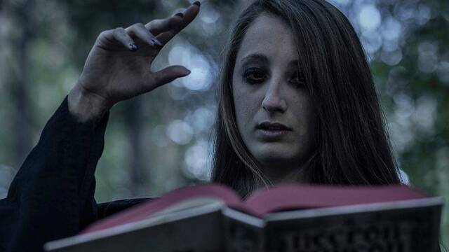 Mujer con aspecto de bruja lee un conjuro.