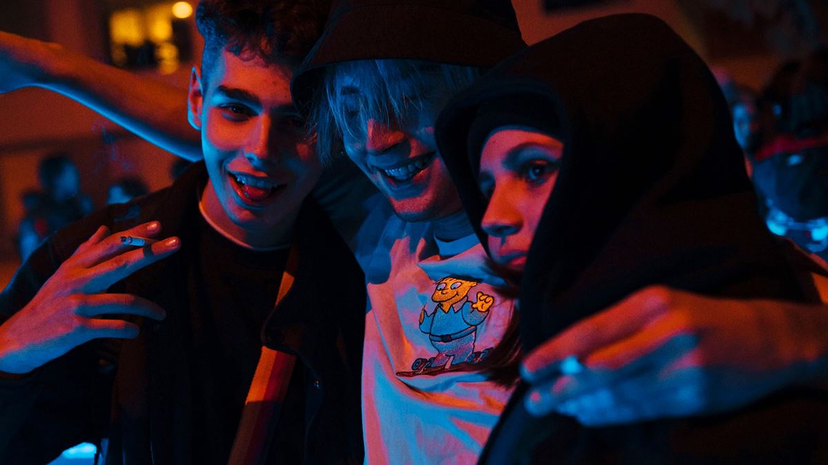 Tres adolescentes abrazados en una fiesta y fumando.