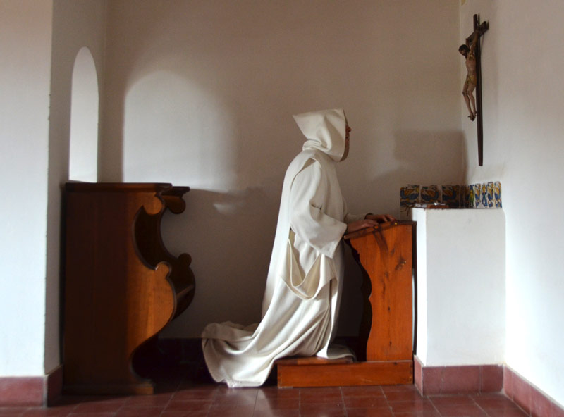 Un cartujo con capucha rezando en su celda
