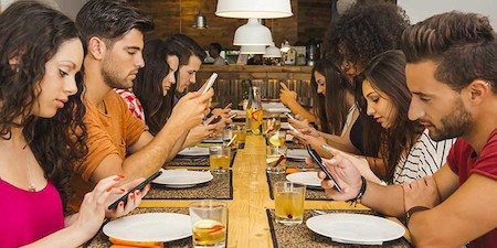 Jóvenes en torno a una mesa, todos mirando el móvil.
