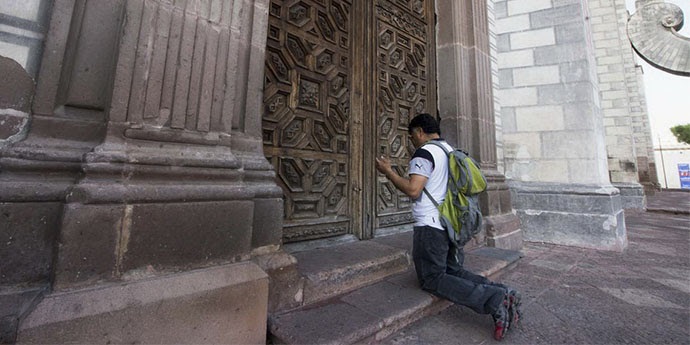 Una persona reza a las puertas de una iglesia cerrada