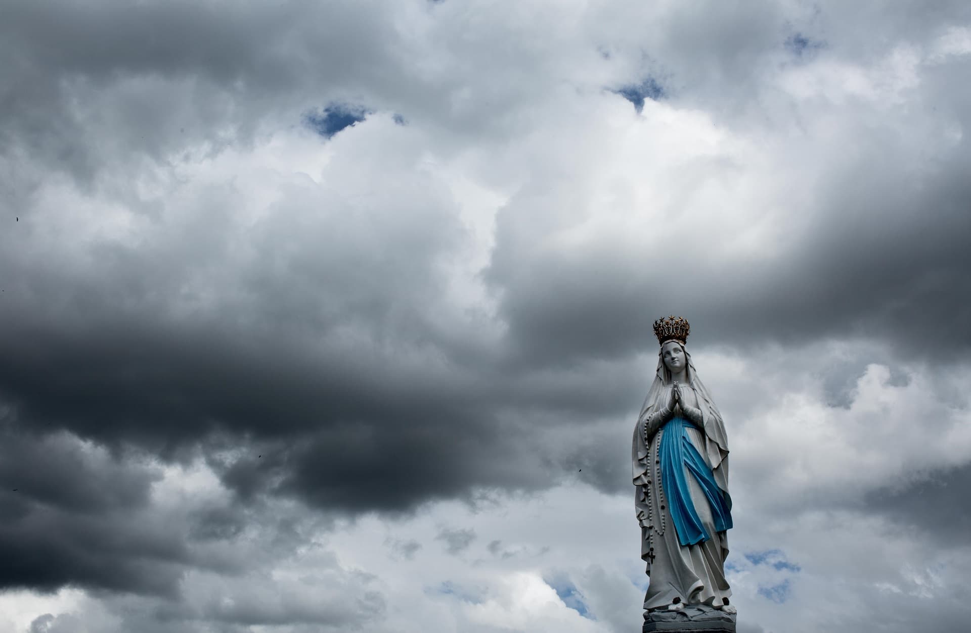 La imagen de la Virgen de Lourdes con un cielo de nubes grises