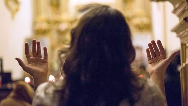 Una mujer alza las manos en oración, gesto frecuente en la oración carismática