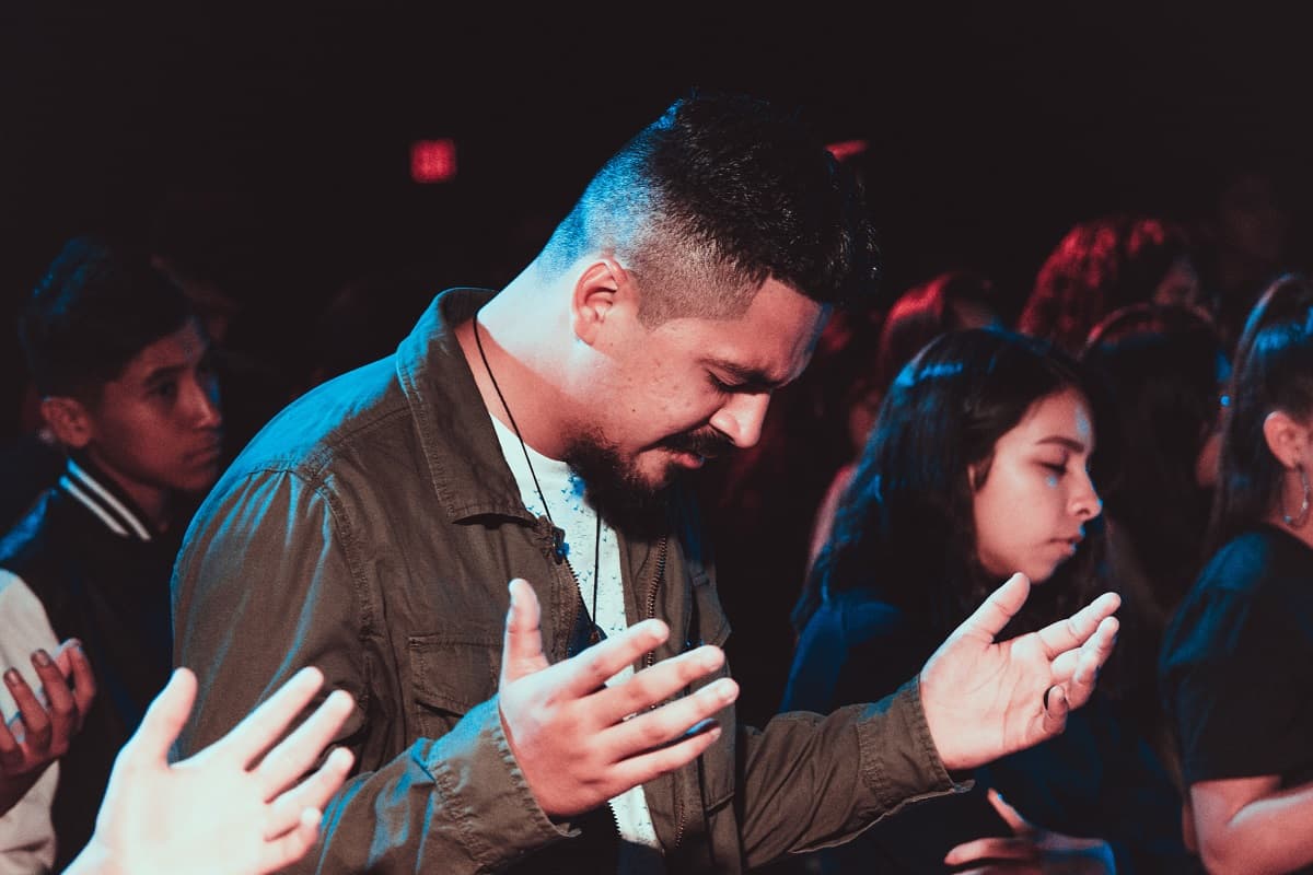 Un hombre alza las manos en oración en un encuentro religioso; foto de Ismael Paramo en Unsplash