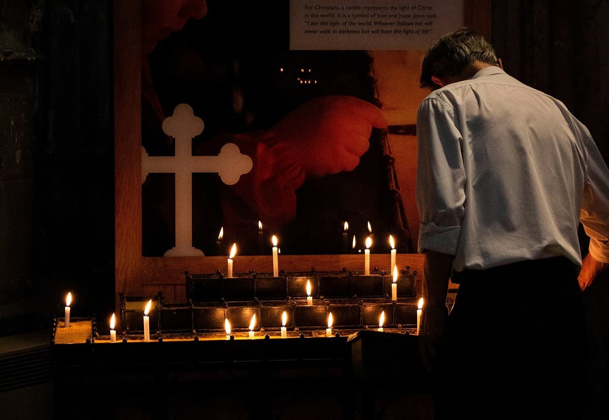 Un hombre trajeado enciende velas en un santuario, foto de Amy Moore para Unsplash