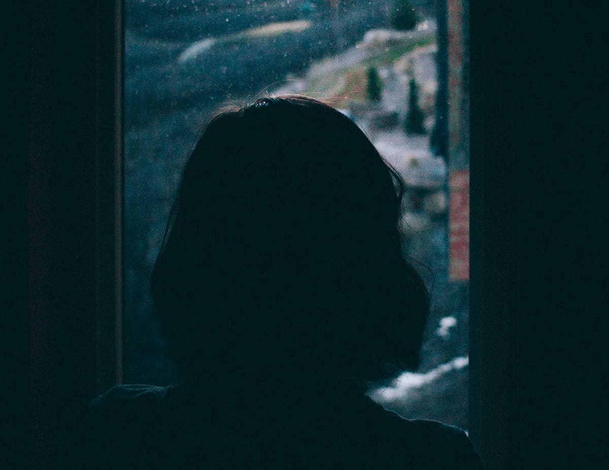 Mujer triste mira nieve y abetos por la ventana, foto de Alec Douglas en Unsplash