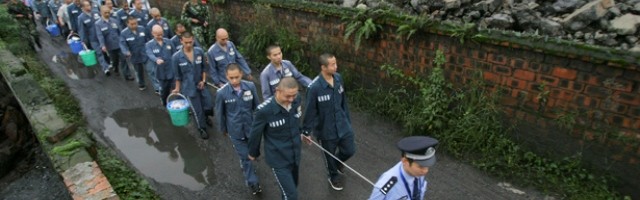 Un policía conduce numerosos presos de un campo de trabajo chino tomados de una cuerda