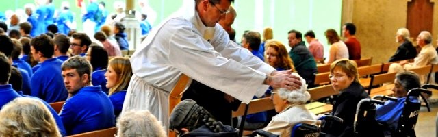 Un sacerdote ora por unas enfermas en silla de ruedas... forma parte de la misión del sacerdote abrazar su vocación sanadora