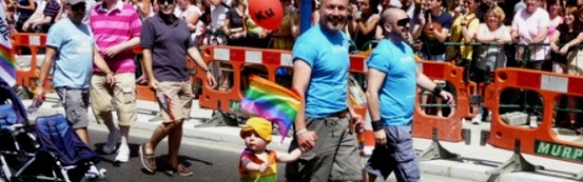 Una pareja homosexual lleva a un niño pequeño con emblemas LGBT a la Marcha del Orgullo Gay