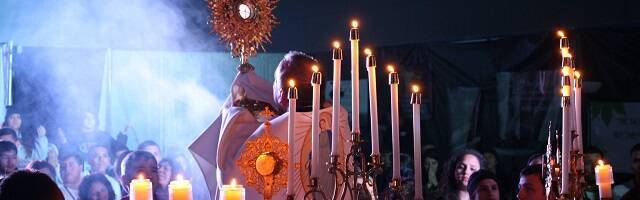 Sacerdote eleva la Custodia en Adoración eucarística con velas, foco e incienso