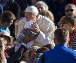 Francisco besa un bebé mientras saluda peregrinos en la audiencia de los miércoles