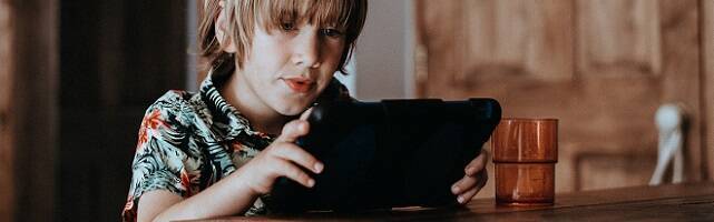 Niño fascinado con una tablet en una mesa de madera