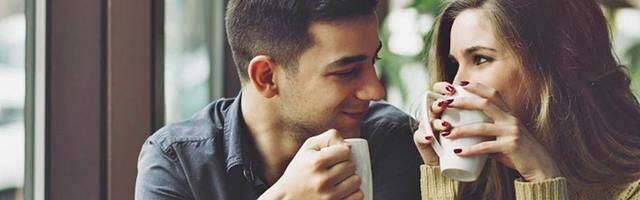 Un chico y una chica se miran mientras sostienen una taza de café.
