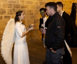 Una voluntaria de Nightfever disfrazada de ángel invita a chicos disfrazados de zombi a poner una vela en la iglesia