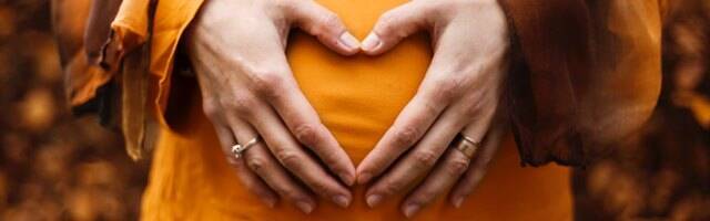 Mujer embarazada marca con las manos un corazón sobre su vientre.
