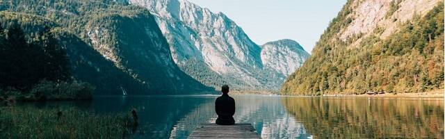 Un hombre sentado junto a un lago e impresionantes montañas