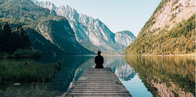 Un hombre sentado junto a un lago e impresionantes montañas