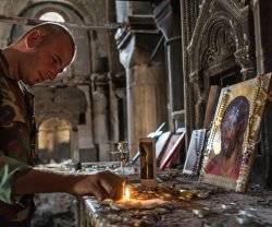 Un cristiano enciende una vela ante un icono de Cristo con rosarios y una vela de San Charbel en una iglesia destruida de Oriente