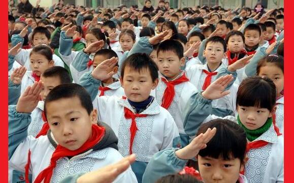 Escolares chinos en formación hacen el saludo comunista con su pañuelo rojo de pioneros comunistas