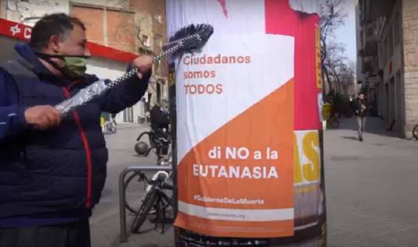 Hombre pegando un cartel de Vividores contra la eutanasia