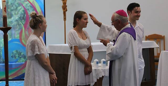 El obispo Breenan unge y confirma a 3 jóvenes revestidos con el blanco del bautismo... en el centro, Hayley, mencionada en el reportaje