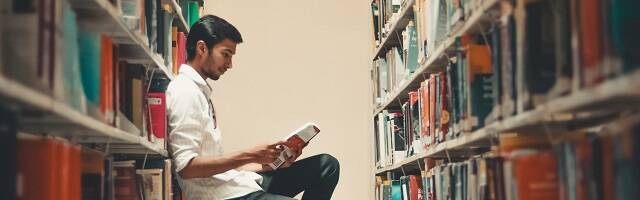 Un joven lee entre las estanterías de una biblioteca - de Dollar Gill en Unsplash