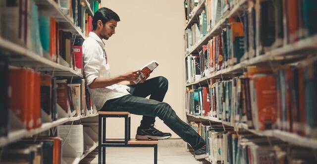 Un joven lee entre las estanterías de una biblioteca - de Dollar Gill en Unsplash