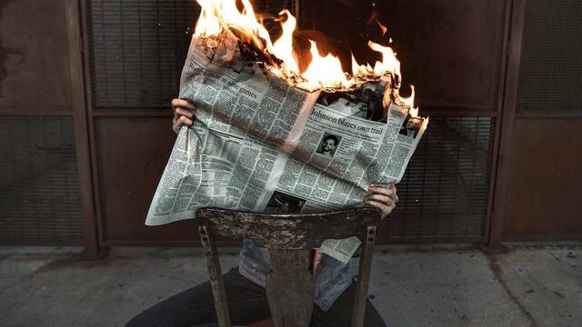 Una mujer sostiene un periódico ardiendo.