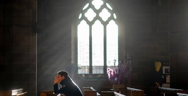 Hombre reza ante ventana de iglesia antigua
