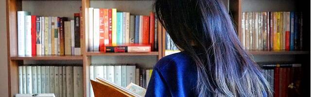 Una joven hojea un libro ante una estantería llena de libros