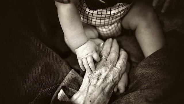 La mano de un bebé acaricia la de un anciano.
