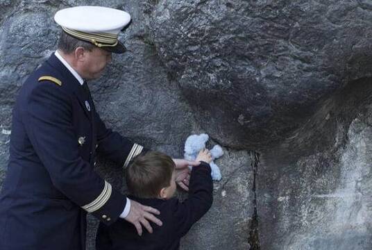 Un militar y un niño con peluche en la gruta de Lourdes