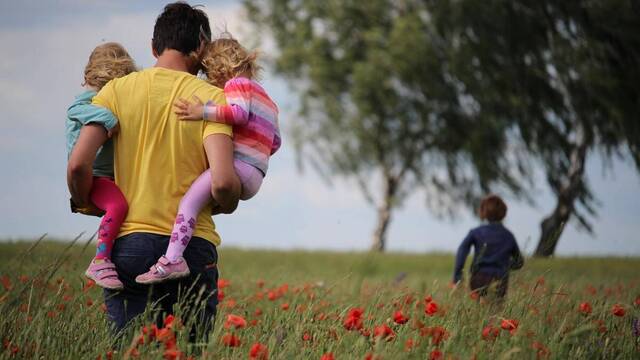 Un padre lleva a dos de sus hijas mientras su hijo corre en el campo.