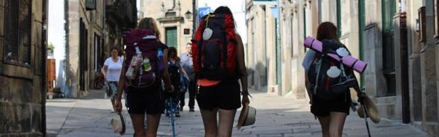Tres jóvenes con mochilas y conchas peregrinas hacia Santiago