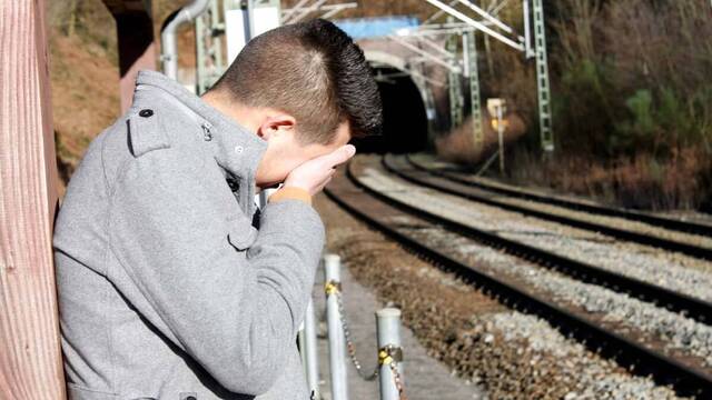 Joven se cubre la cara por tristeza ante la vía del tren.