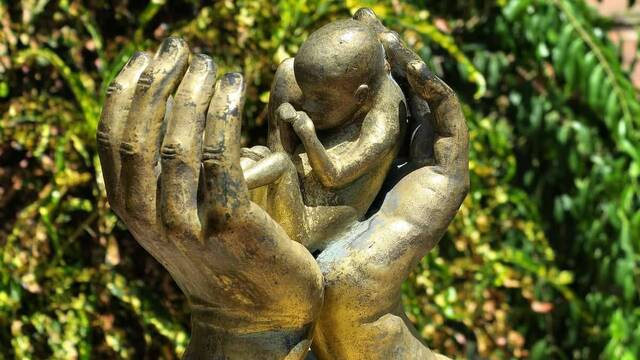Escultura de unas manos con un feto.