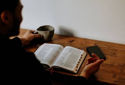 Un hombre lee la Biblia mientras toma una bebida, foto de Priscilla Du Preez en Unsplash