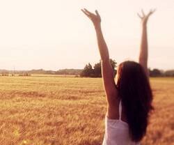 Una joven alza los brazos en actitud de alabanza en un campo soleado