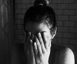 Mujer llorando en la ducha se tapa la cara.